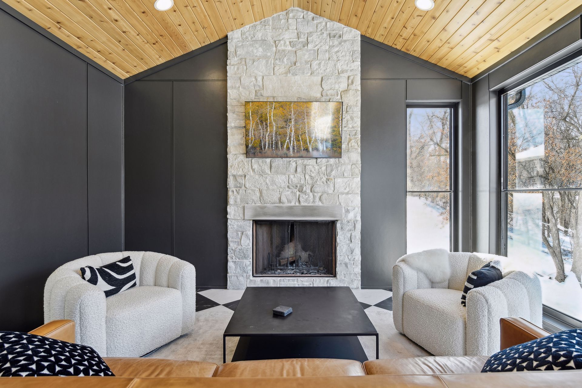 Four-season porch with vaulted cedar ceiling, stone fireplace and boucle armchairs