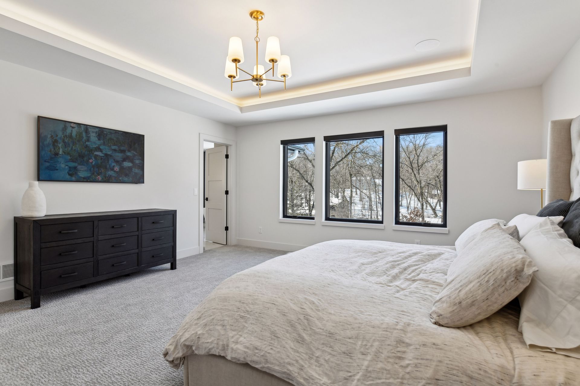 Primary suite with tray ceiling, brass chandelier and black-framed windows
